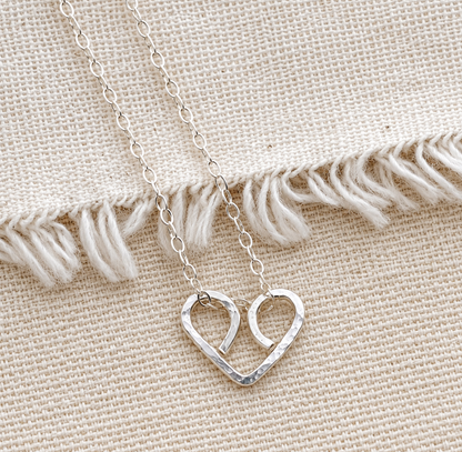 A close-up shot of dainty, handmade gold looped wire heart necklace on a fabric.