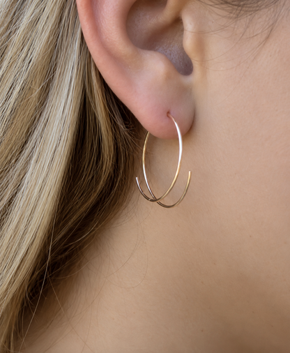 A close-up of a person's ear wearing a delicate, thin gold hoop earring with a second, larger gold hoop layered behind it.