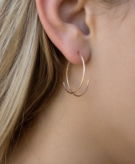 A close-up of a person's ear wearing a delicate, thin gold hoop earring with a second, larger gold hoop layered behind it.